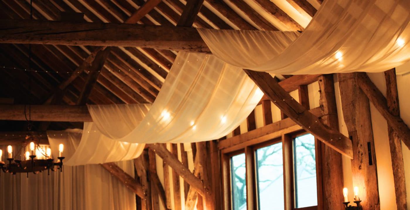 Fabric draped across the oak beams of the barn ceiling, lit warmly for the day