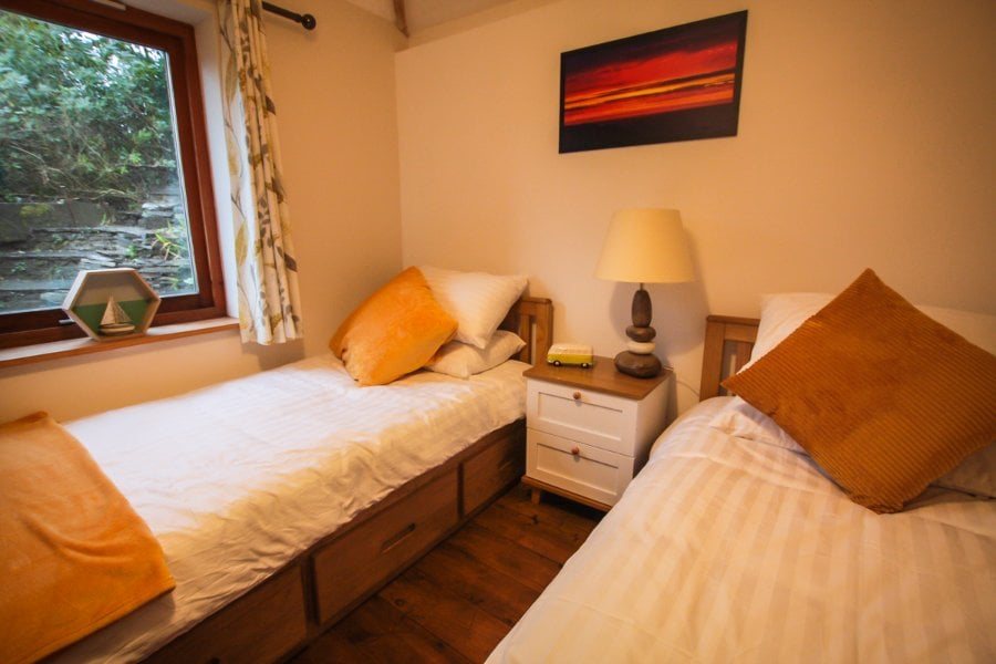 A twin bedroom with wooden bed frames, warm bedding and a window onto greenery