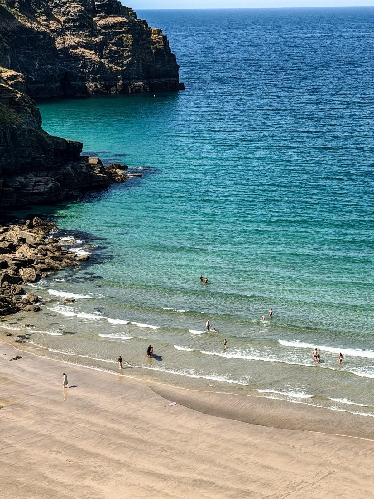 Turquoise Atlantic water and cliffs at a North Cornwall cove, with swimmers in the shallows
