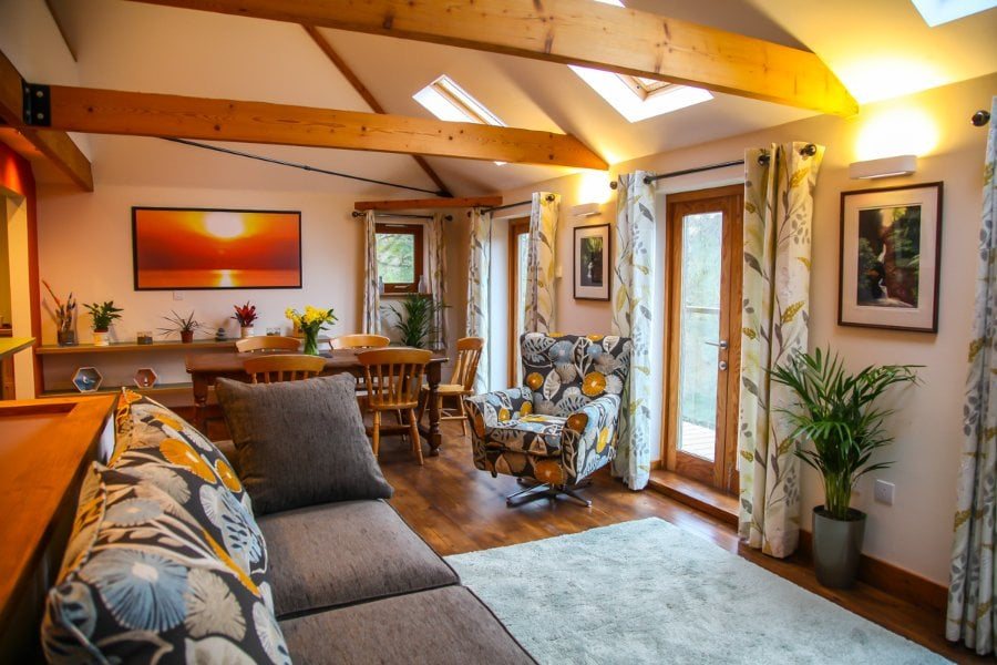 An open dining and sitting room under pine beams, with a long table and garden doors