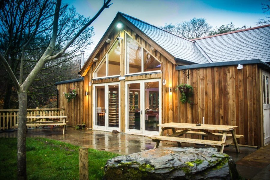 The lodge lit from within at dusk, with picnic benches on the terrace outside