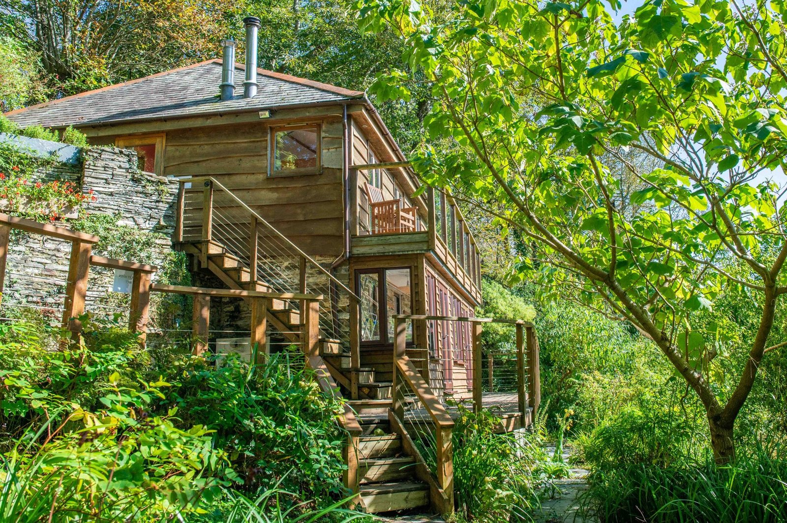 The timber and stone retreat lodge in sunlight, framed by trees and a wooden staircase