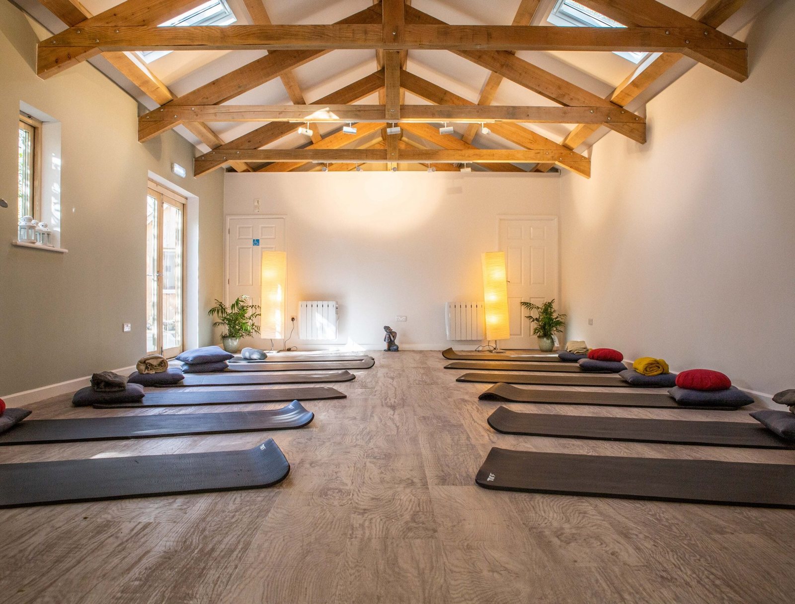 A light barn studio with exposed oak beams, mats and cushions laid out in two rows